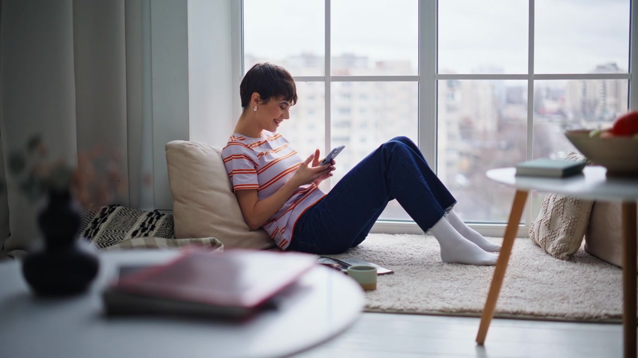 Laughing girl watching smartphone funny online content sitting home floor.