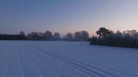 Aerial-establishing-shot-of-a-rural-landscape,-countryside,-agricultural-fields-and-trees-covered-with-snow,-cold-freezing-weather,-sunset-golden-hour-light,-wide-ascending-drone-shot-moving-forward