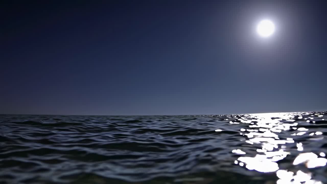 Low-angle video capturing a serene ocean under a bright moon, reflecting light on the water's