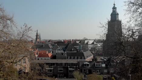 Slow-forwards-aerial-showing-medieval-city-center-of-Zutphen,-The-Netherlands,-against-a-blue-sky-with-the-Walburgiskerk-church-tower-and-Wijnhuistoren-rising-above-the-historic-rooftops