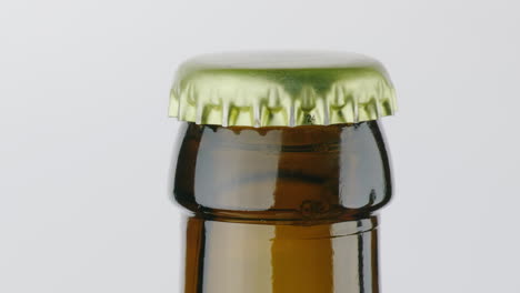 the neck of a bottle of beer is covered with a metal lid on a white background