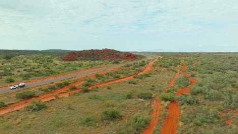 aerial flyover australian outback red dirt and bush trail with buggy racing alongside rural highway, 4k drone