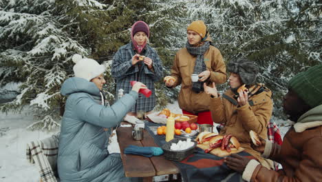 friends eating bbq food at table in winter forest