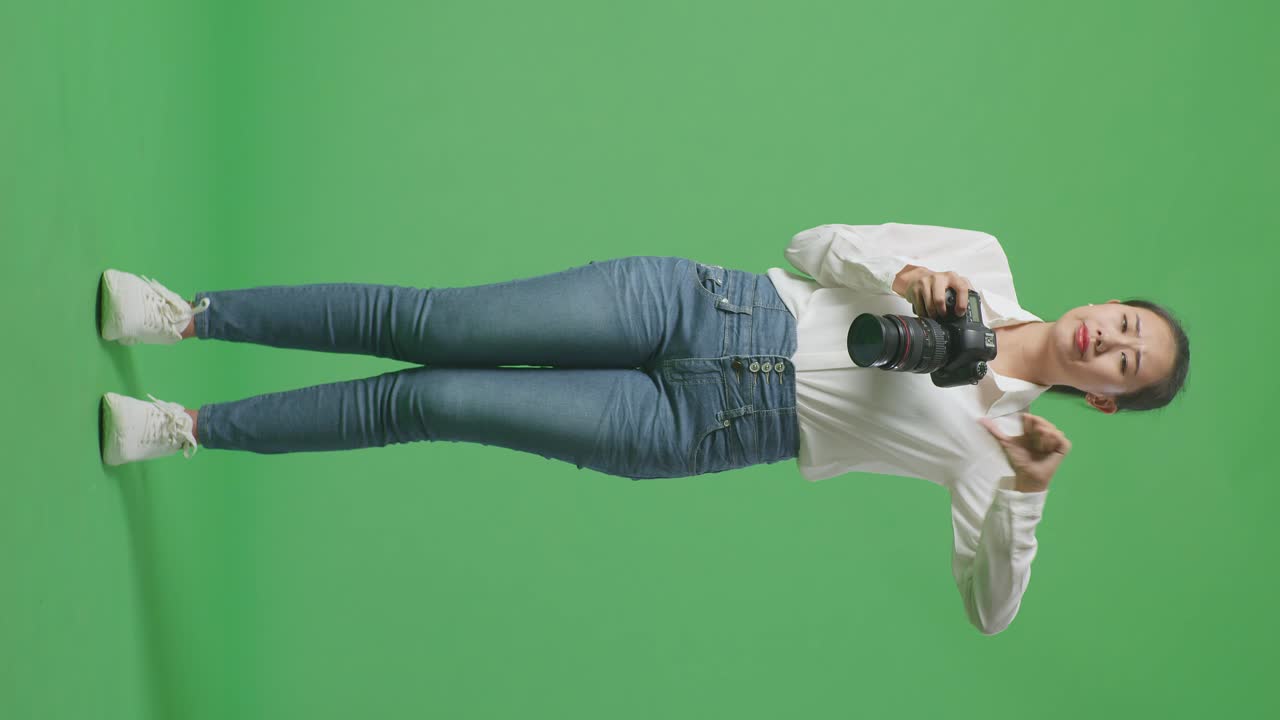 화가 난 아시아인 사진작가는 카메라를 이용해 사진을 찍고, 그 다음에는 스튜디오의 녹색 스크린 배경에 서서 엄지손가락을 아래로 는 제스처를 보여준다.