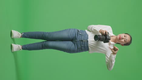 cuerpo lleno de fotógrafo asiático molesto usando una cámara tomando una foto y luego mostrando los pulgares hacia abajo gesto mientras estaba de pie en el fondo de la pantalla verde en el estudio