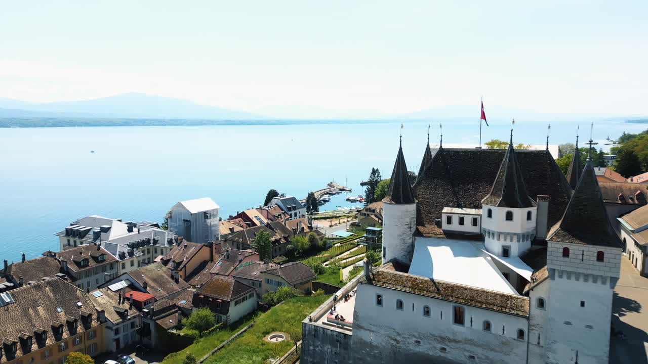 Aerial: Nyon Castle at midday with Lake of Geneva in canton of Vaud, Switzerland, pull out drone shot