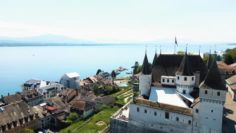 aerial: nyon castle at midday with lake of geneva in canton of vaud, switzerland, pull out drone shot