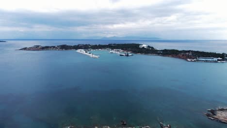 High-angle-drone-shot-of-beautiful-peninsula-with-marina-during-a-calm-cloudy-afternoon-in-Laimos-area-in-Vouliagmeni,-Greece-|-4K