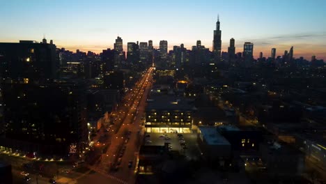 A-captivating-drone-aerial-view-of-a-Chicago-at-dusk,-showcasing-illuminated-skyscrapers-against-the-darkening-sky-The-golden-hues-of-sunset-paint-a-serene-backdrop,-highlighting-architectural-marvels