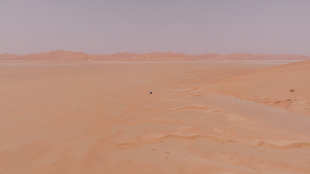 Car in the endless desert landscape in Oman, featuring isolated terrain and a lone object