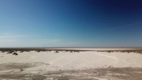 Aerial,-low-angle-flyover-of-isolated-sand-dunes-with-some-vegitation-on-barrier-island-on-the-Texan-Gulf-of-Mexico-coast-on-a-bright-sunny-afternoon---South-Padre-Island,-Texas