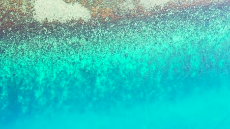 Flyover-the-aquamarine-seawater-with-a-coral-reef-approaching-beautiful-beach-with-granite-boulders