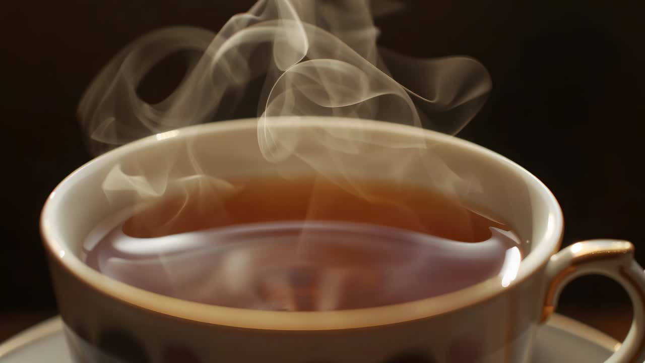 Displaying porcelain teacup gold rim with steam curl rising from hot tea on wood table, reflections