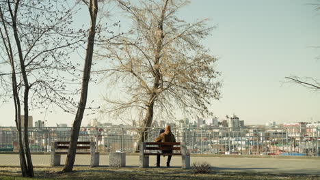 a father carrying his son on his leg as they sit together on a park bench, looking out at the cityscape, the father adjusts his position on the bench while holding