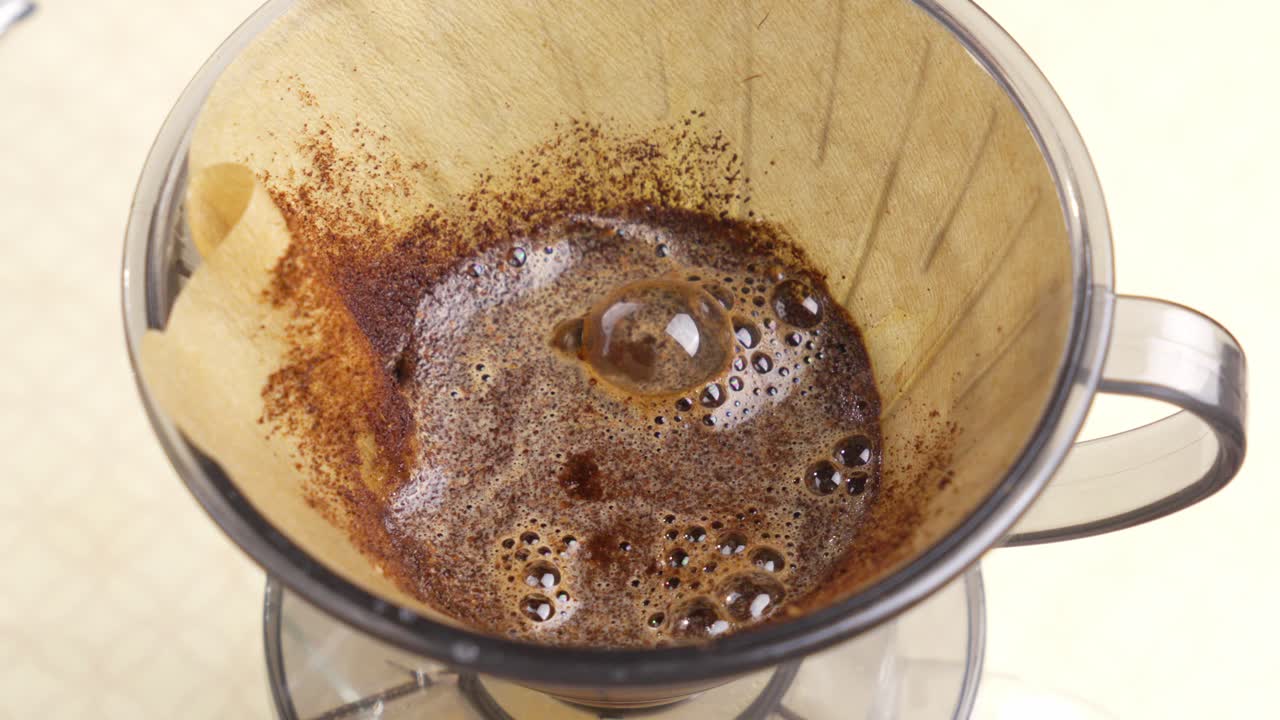 Varm kaffe som drypper og bobler gjennom papirfilter under pour over-ekstraksjon, statisk medium oversikt