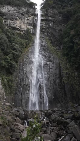 nachi waterfall tumbling gracefully over rocky outcrop surrounded by lush green vegetation. slow motion, vertical video