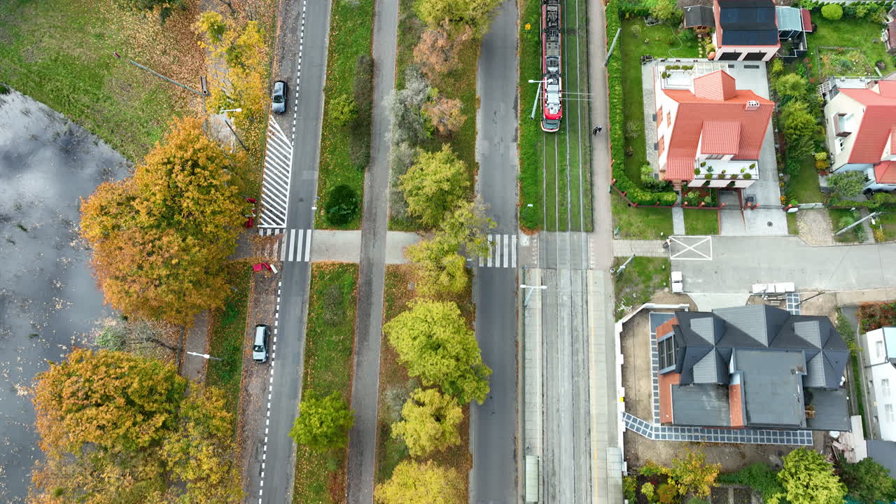 Top-down drone view of tram and cars moving along a tree-lined street in Gdańsk during autumn