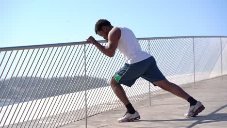 athletic smiling man leaning at fence and stretching