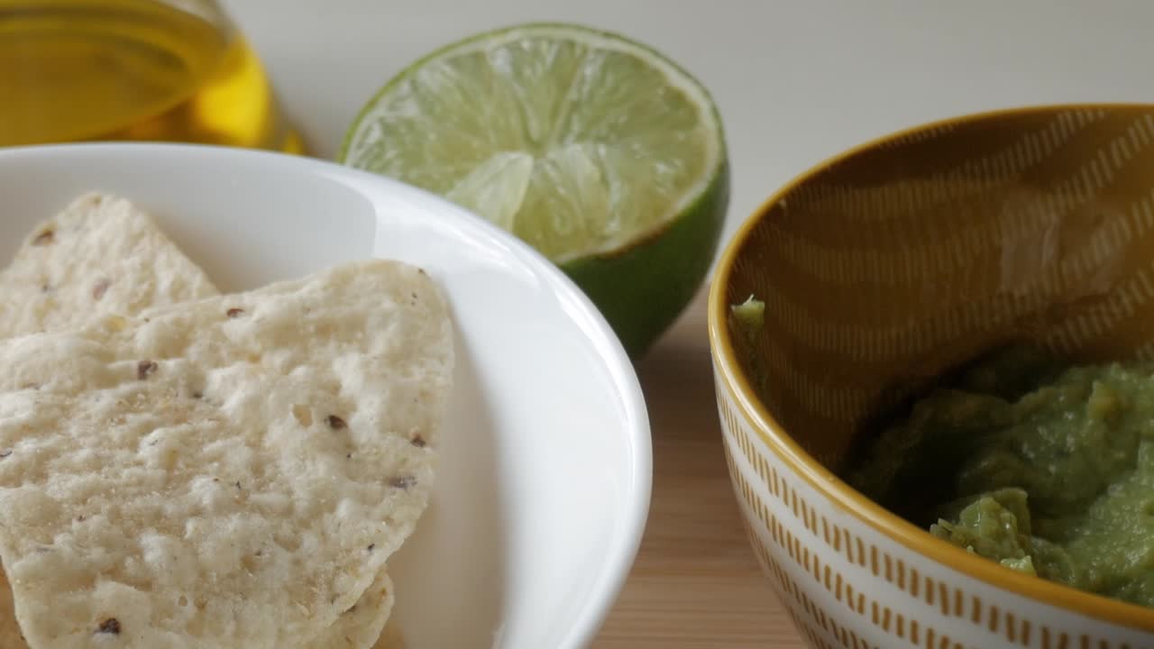 Fresh guacamole in bowl with tortilla chips and lime, cozy kitchen snack setting