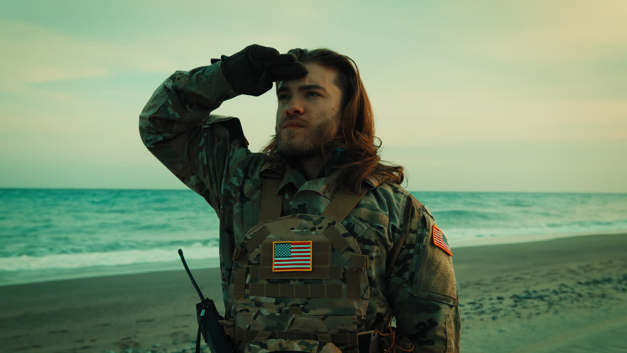 Amerikansk soldat med langt hår hilser på en strand nær havet på Memorial Day