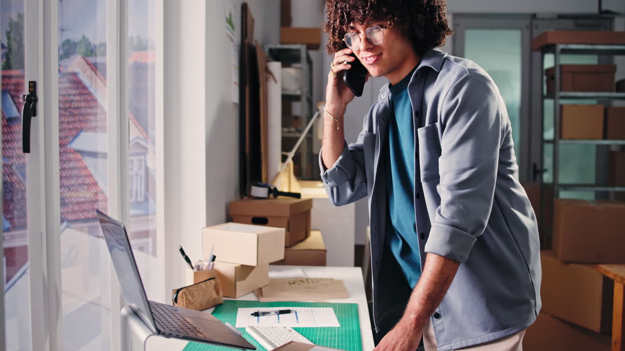 Jonge man die aan het telefoneren is terwijl hij op een laptop werkt op kantoor