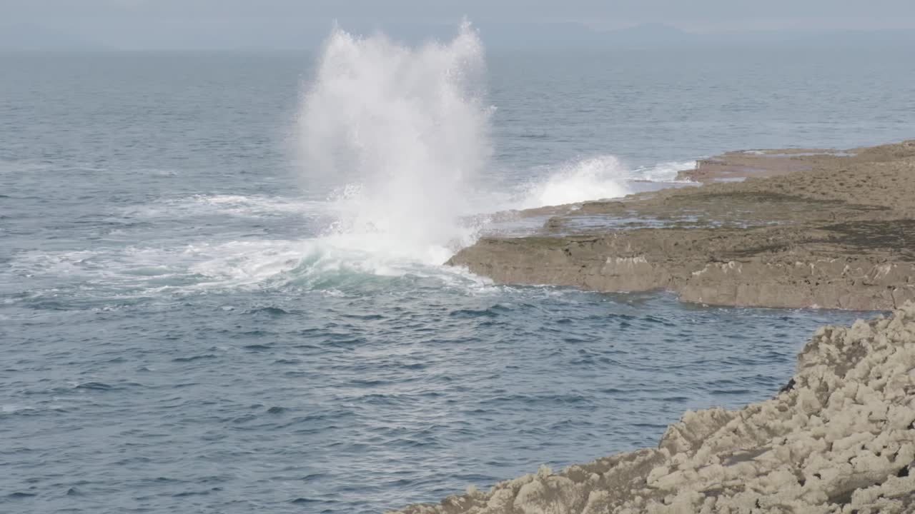 Ocean waves breaking on rocky cliffs coast and splashing very high leaving foamy white stirred water. Rocky shore as part of Irish coastline near Doolin.