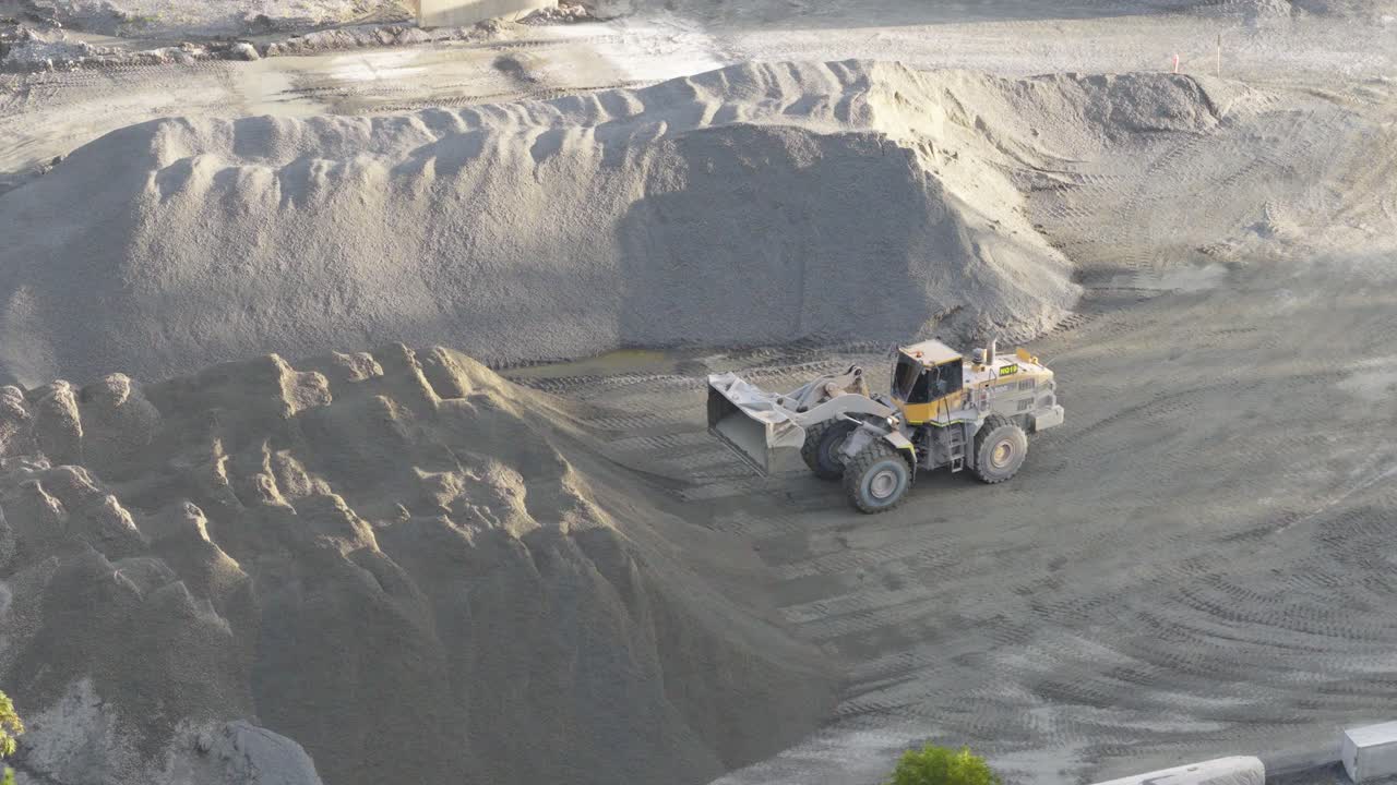 Aerial footage of a loader moving sand in a Gold Coast quarry. Bright daylight highlights the machinery and terrain