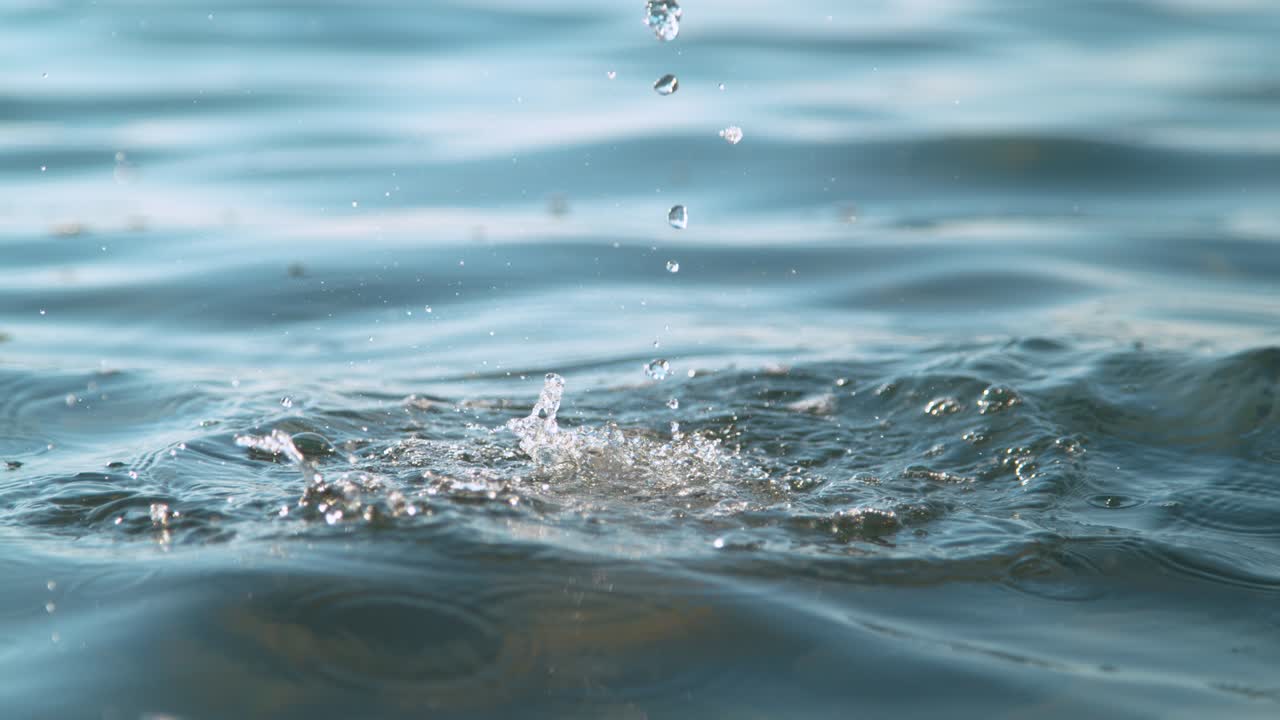 CLOSE UP, DOF: Droplets of crystal clear liquid fall into the tranquil ocean.