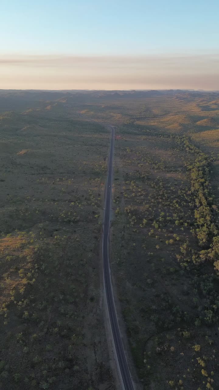 Aerial reveal of a solitary road stretching through the outback at golden hour, captured in the Northern Territory.