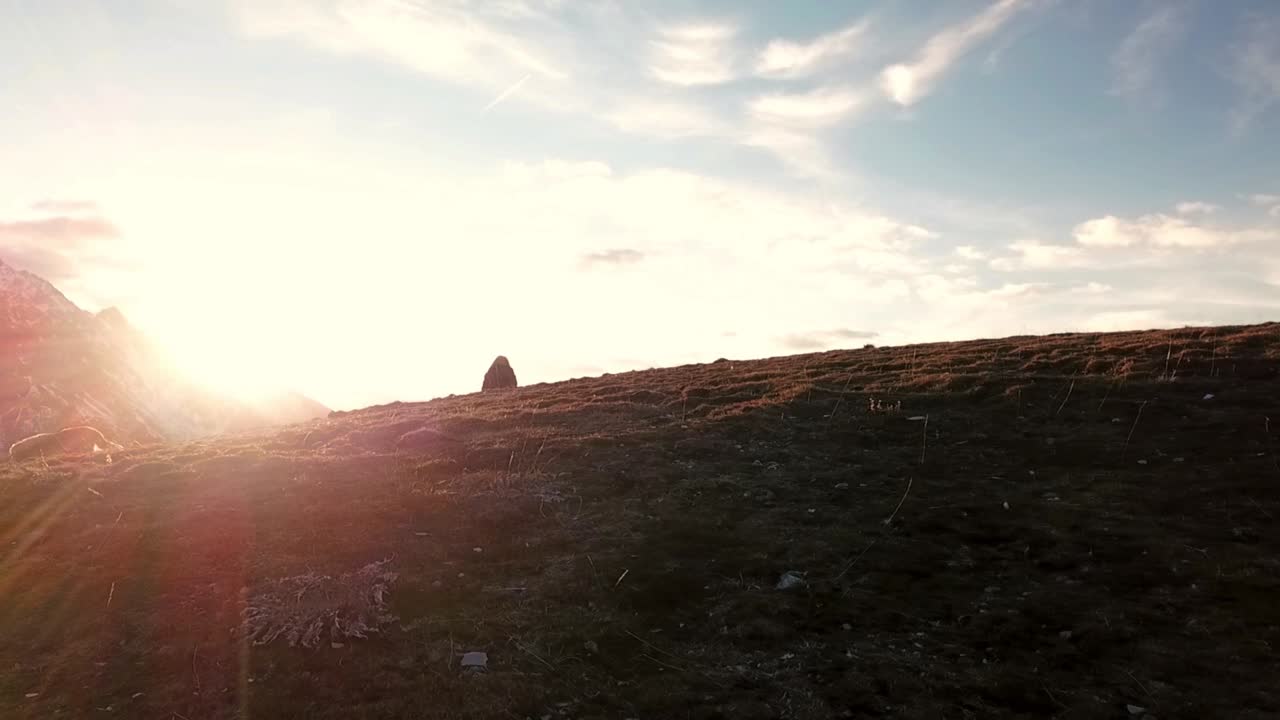 drone view of a woman sitting on a hill looking at an epic mountain scenery oh her travels during the summer in the sunset