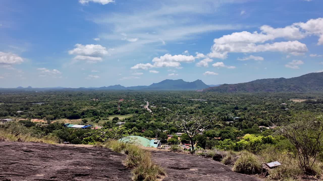 View of Dambulla rural landscape, showcasing lush greenery and distant mountains under a clear blue sky in Sri Lanka. Pan Left Shot