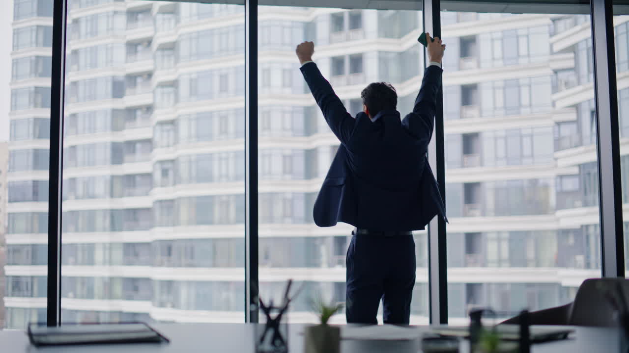 Entrepreneur celebrating cellphone news standing by building panoramic window