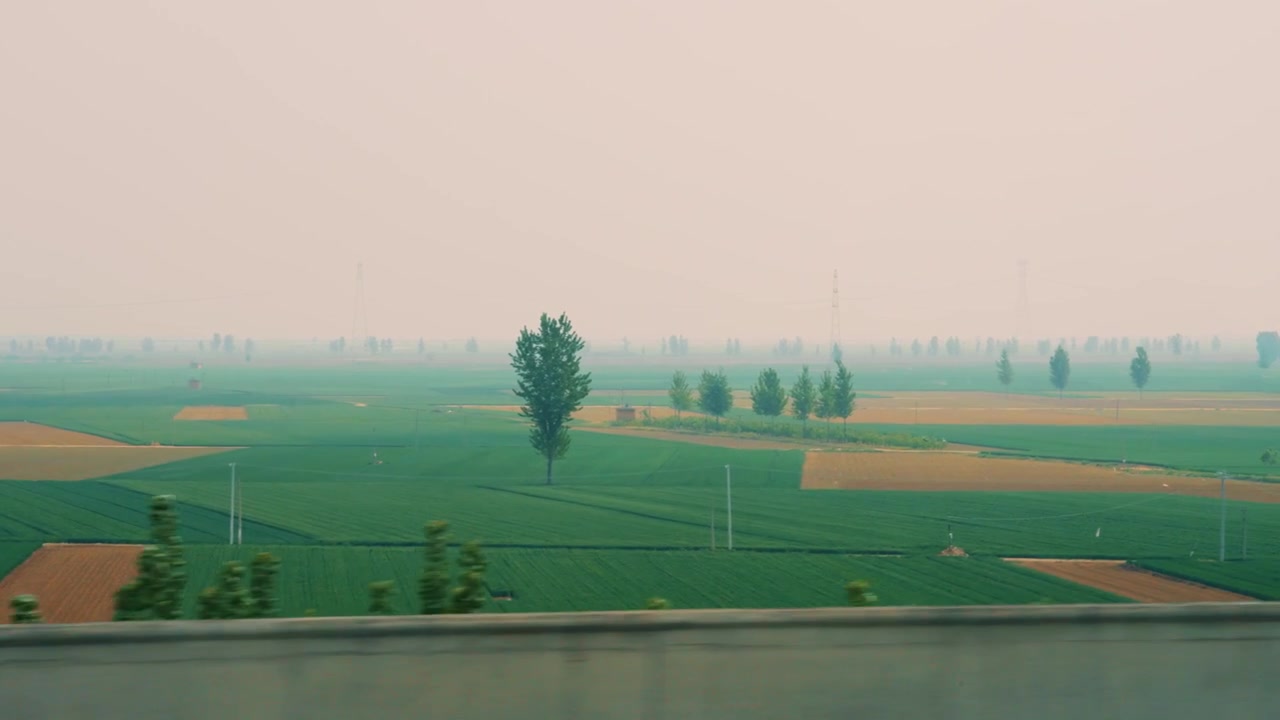 Una ripresa in soggettiva fluida e in movimento di ampi campi coltivati vicino a Xi'an, Cina. Campi geometrici verdi e marroni si estendono verso un orizzonte lontano e velato, costellato di alberi sparsi e linee elettriche.