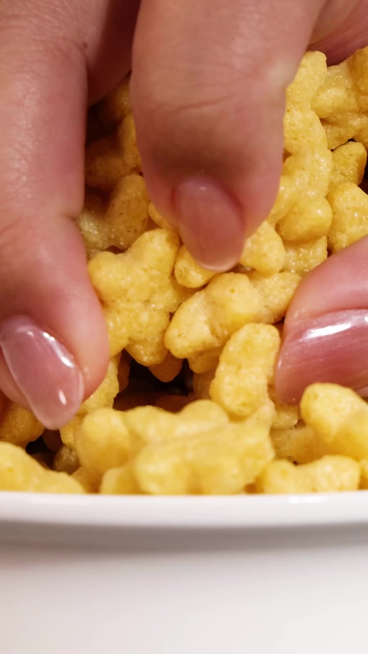 Una mano si allunga in una ciotola di cereali a forma di stella su sfondo nero, creando un'esperienza tattile e ravvicinata.