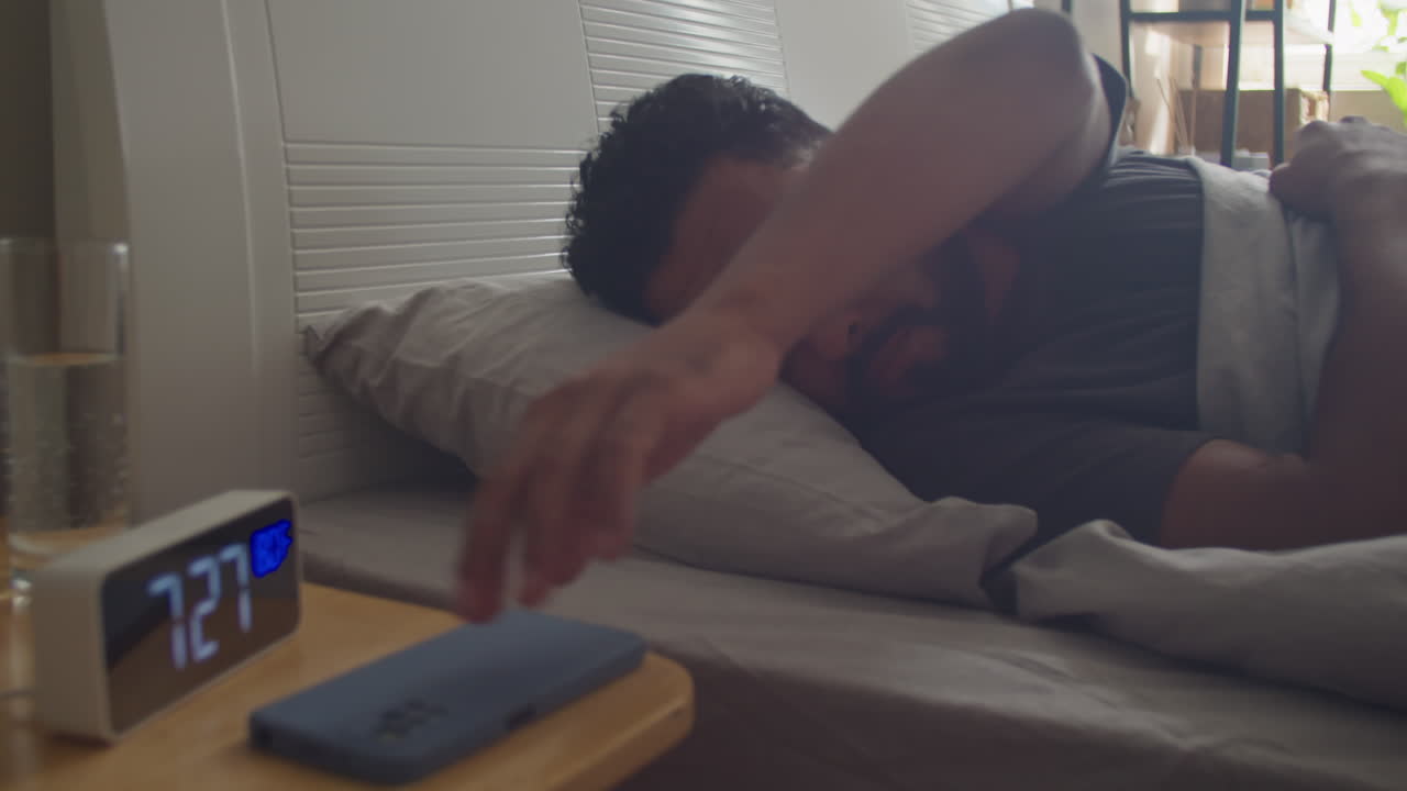 Man Waking Up in Bed and Taking Smartphone