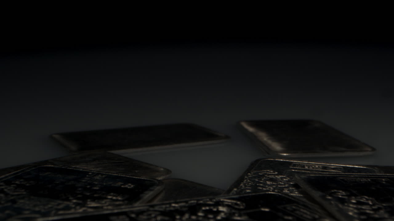 Cinematic macro dolly in of a large amount of silver bars lit by a large spotlight against a dark background