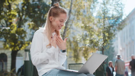 mujer joven sentada en la calle de la ciudad mirando la cámara portátil haciendo videoconferencia con cámara web