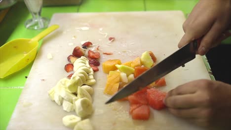 male hands chopping fruits on board to prepare a cocktail of fruits