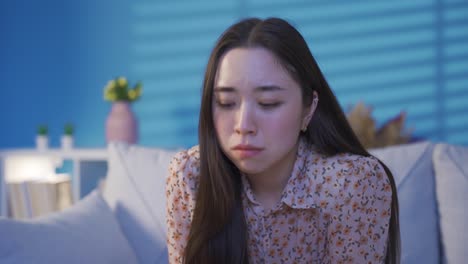 thoughtful depressed asian young woman sitting alone on sofa at home.