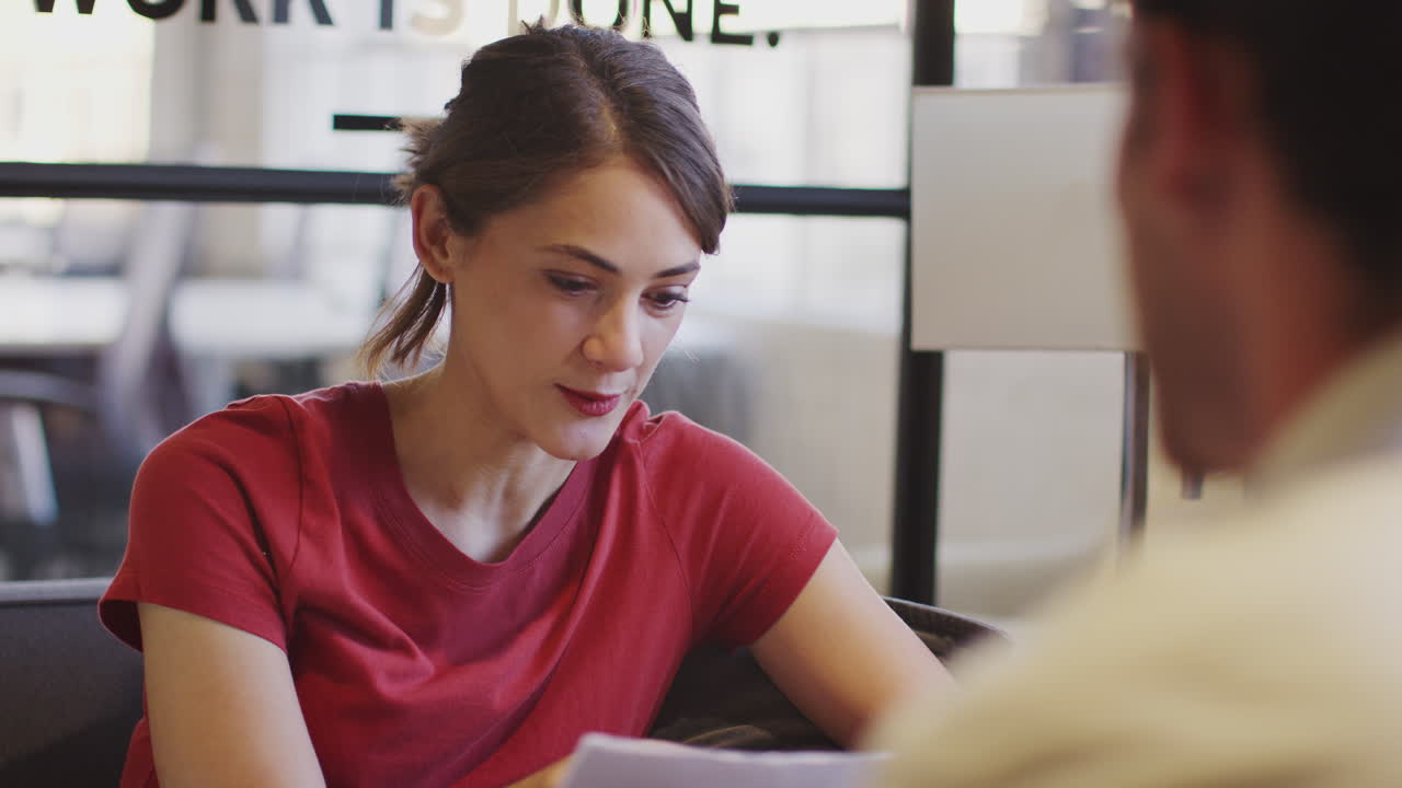mujer de negocios hablando con un colega masculino en una sala de reuniones, por encima de la vista del hombro