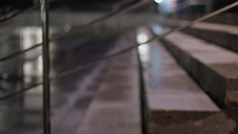 close-up view of a staircase with a metal handrail, with blurred view of cars passing across the road at night, illuminated by soft lighting