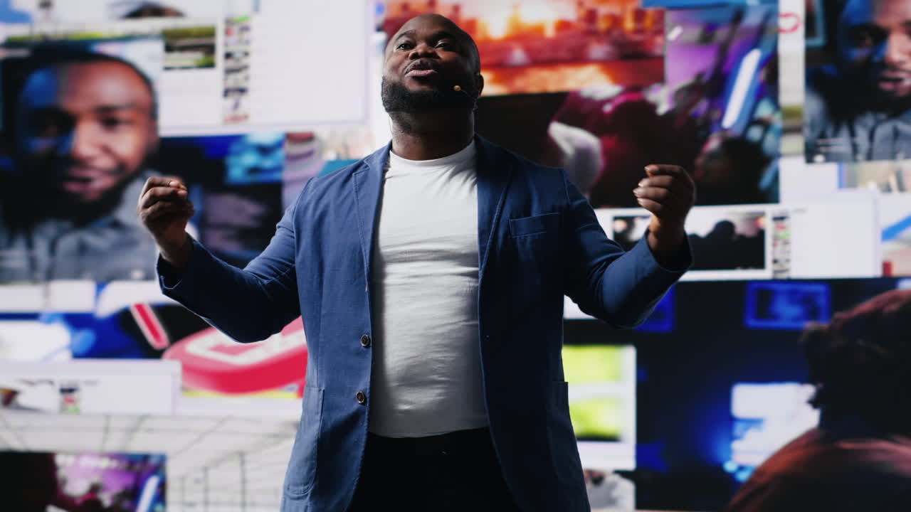 African American public speaker on stage surrounded by digital visuals