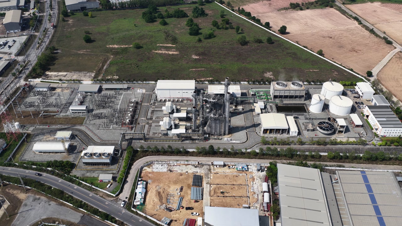 Expansive aerial view of a large industrial power plant complex, showcasing the infrastructure, storage tanks, and surrounding area with ongoing construction and development activity