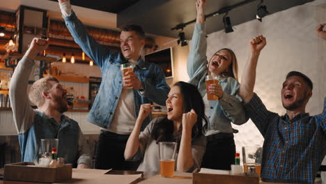 Friends-watch-football-together-on-TV-in-a-bar-and-celebrate-the-victory-of-their-team.-Shout-with-joy-and-dance.-Emotions-from-victory