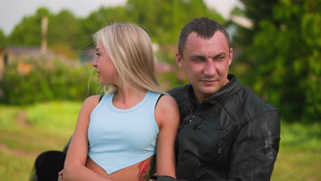 Attractive-woman-and-biker-sit-on-motorcycle-in-village