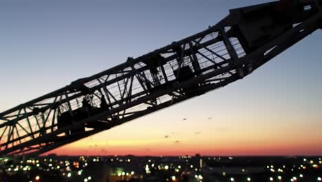 a majestic crane silhouetted against a beautiful twilight skyline, capturing the transition from day to night with soft hues of sunset and city lights sparkling below