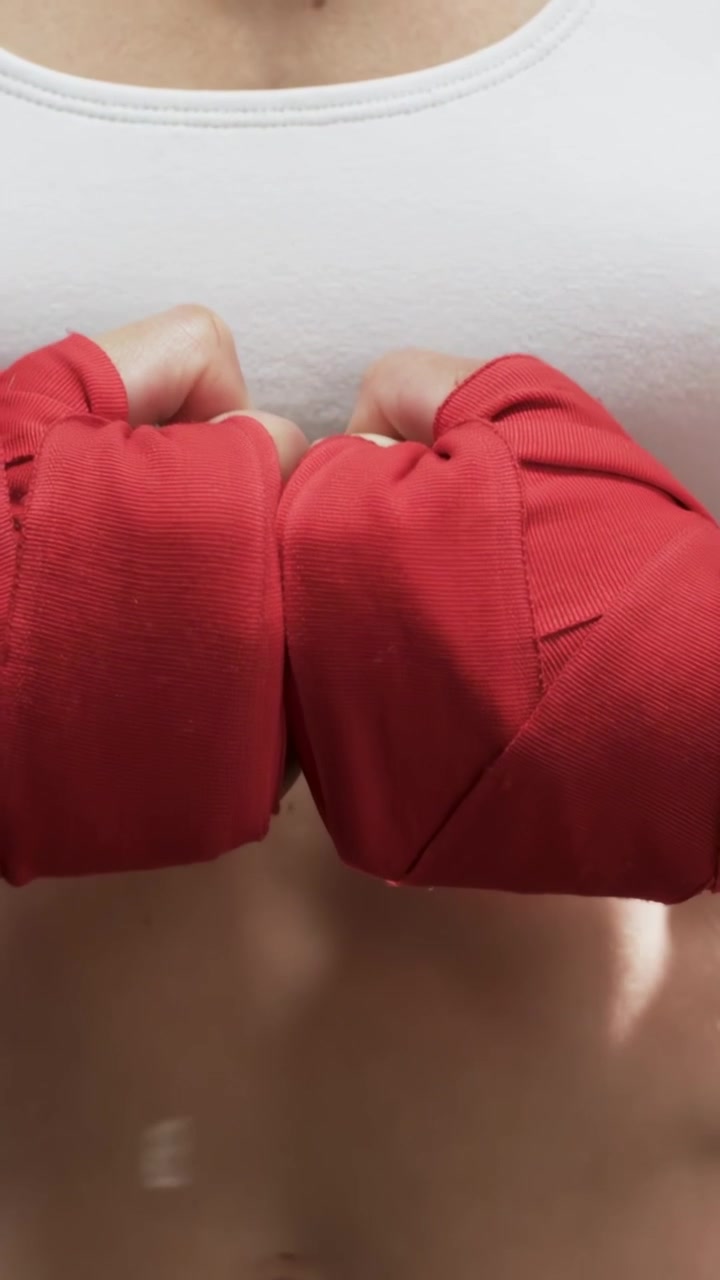 Video verticale: Pugile che sistema le fasce rosse al polso sinistro, stringendo i pugni sotto un flusso AR per il fitness.
