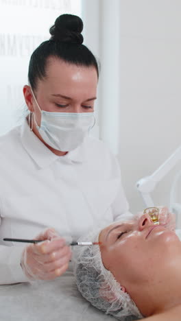 terapia enzimática esteticista aplicando crema médica hidratante en la cara de una mujer joven con un pincel