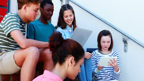 grupo de amigos de la escuela sonrientes en la escalera usando computadora portátil y tableta digital