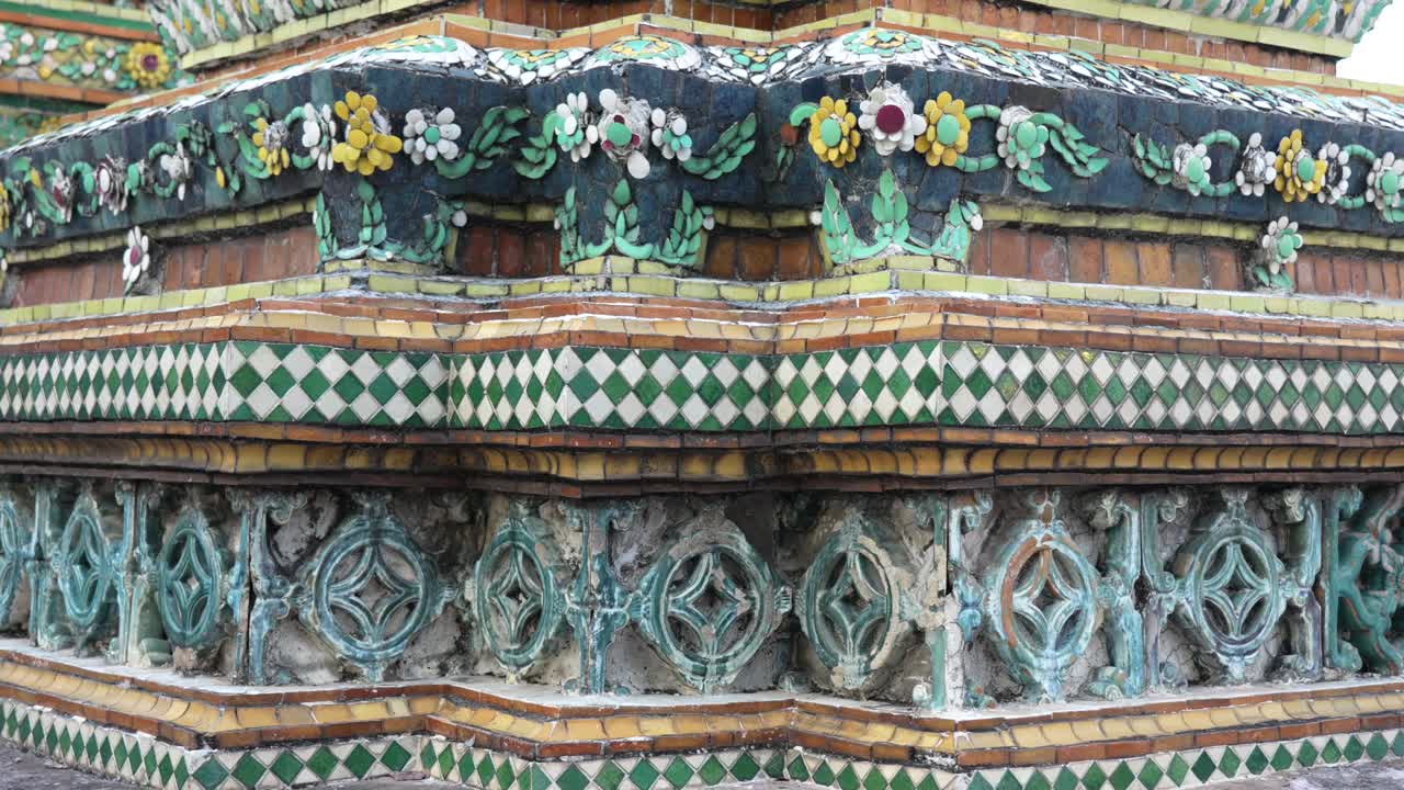 Wat Pho chedi exterior showcasing detailed traditional Thai temple architecture with colorful mosaic tiles, creating vibrant floral and geometric patterns in Bangkok, slow motion panning shot